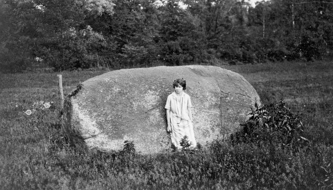 A black and white photo of a person standing in front of a large boulder