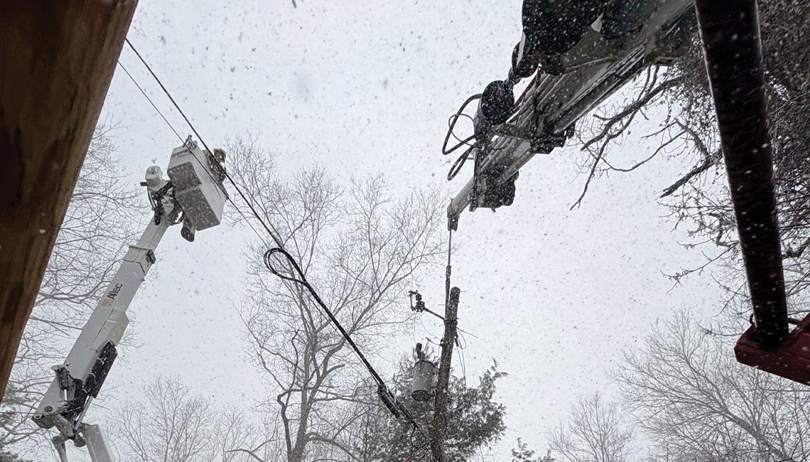 An upward view of linemen working on power lines in the snow
