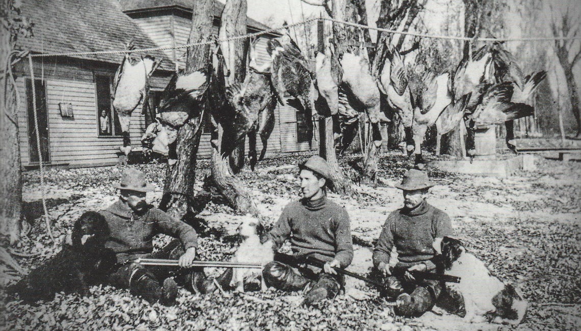A black and white image of men sitting on the ground with guns after a duck hunt