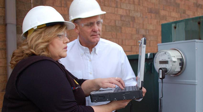 Lisa Queen and Kevin Kemmerer wear hard hats and look at a computer.