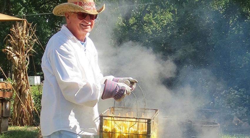 A man cooks a basket of corn on the cob at a festival.