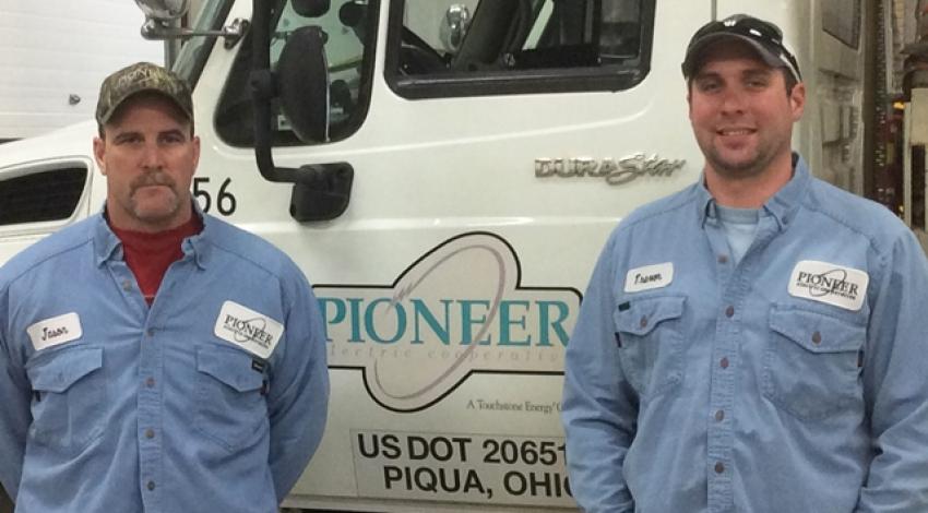 Lineworkers Jason Woods and Trevor Lavy smile for a picture beside a Pioneer Electric truck.