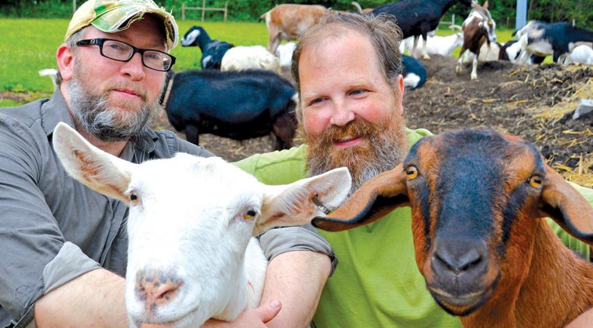 Chad Snelling and Jeff Wince smile for a picture with two goats.