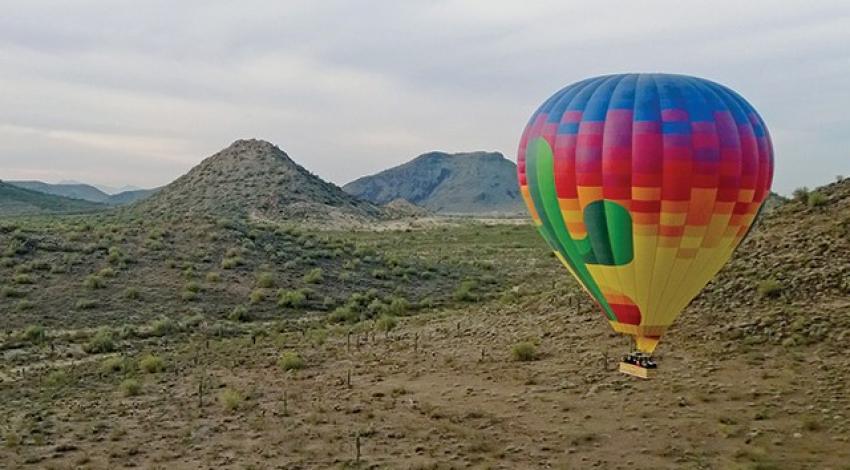 A rainbow-colored hot air balloon flies over the desert.