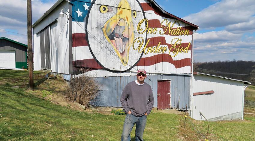 Scott Hagan poses beside a barn he painted as an American flag and eagle.