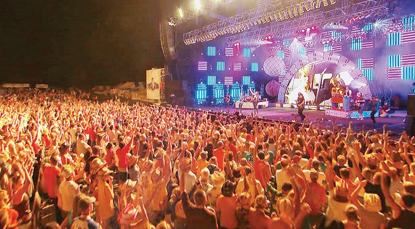 A large crowd celebrates and dances in front of a stage