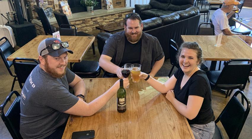 Three people smiling around a table enjoying drinks
