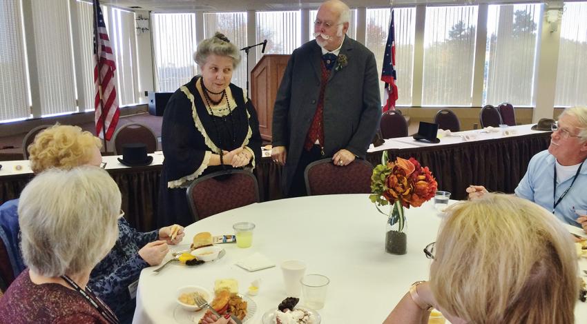 A group sits around a table as two impersonators visit with them.