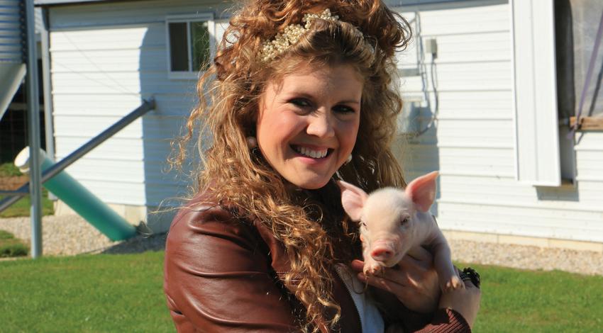 Lauren Schwab Eyre holds a baby pig and smiles for a picture.