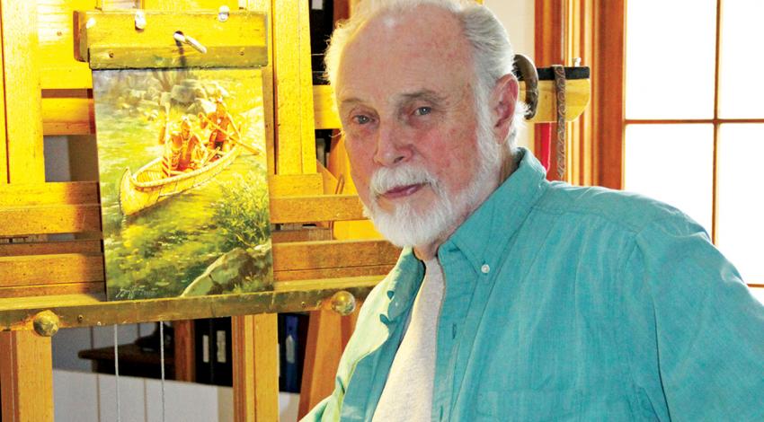 Robert Griffing looks into the camera as he sits next to a piece of his art depicting a canoe.