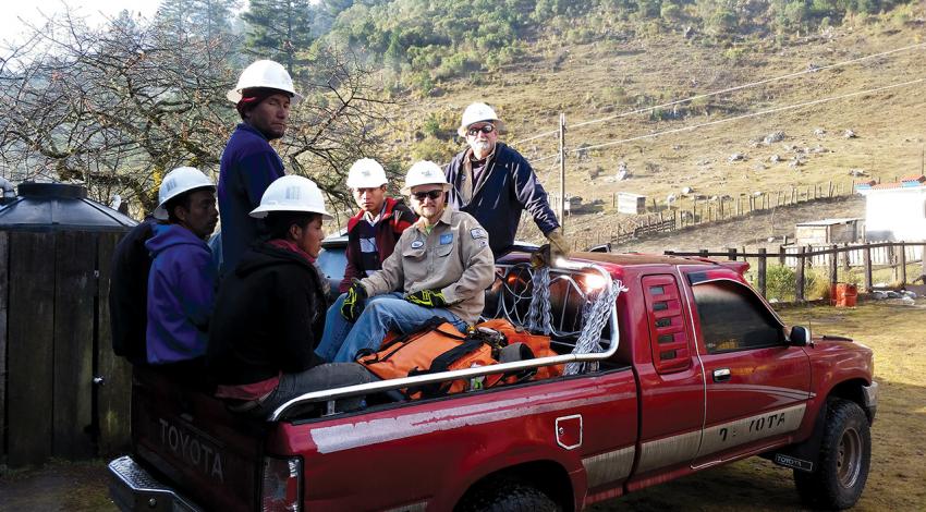 A group of workers sit in the back of a pickup truck.