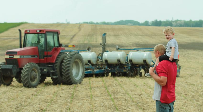 Casey Longshore and his son, Landen, stand in a field beside a tractor.