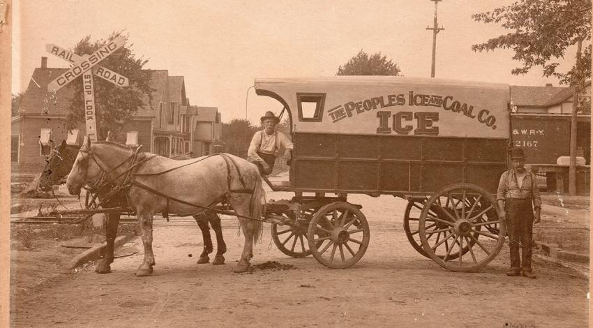 Two men pose with a wagon drawn by horses, designed to carry and deliver ice.