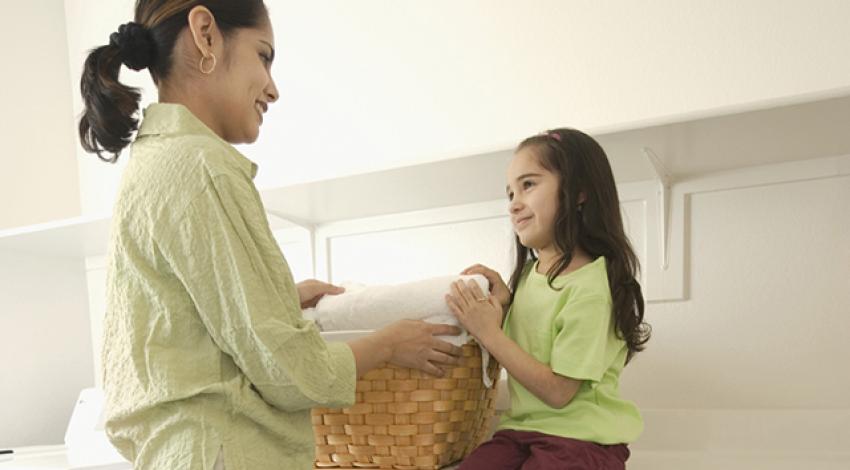 A woman and her daughter hold a basket of laundry.