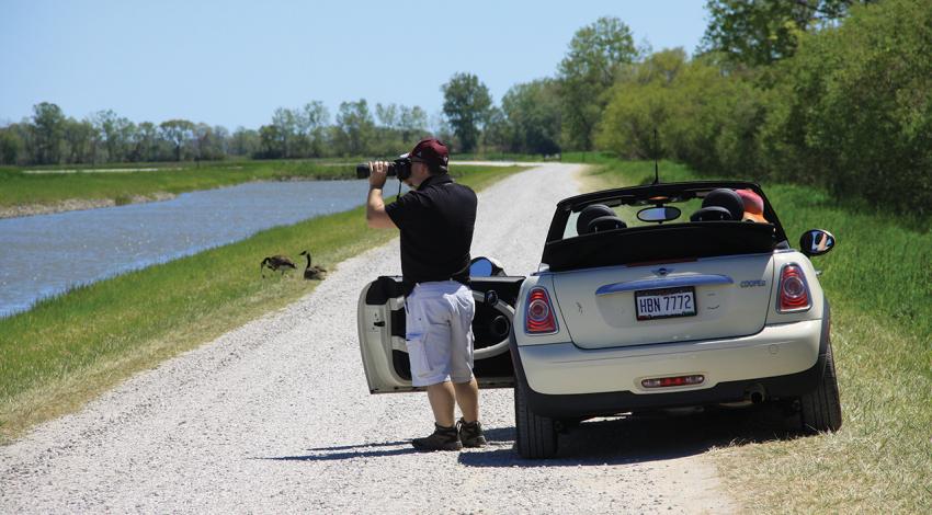 A bird-watcher stands next to his car and looks through a camera.