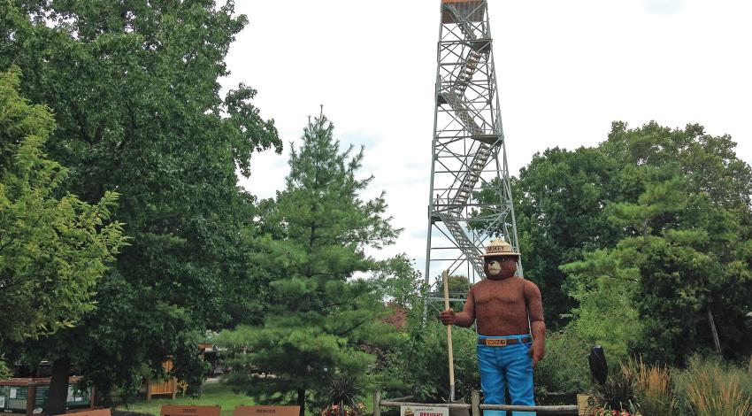 A 15-foot-tall statue of Smokey Bear standing in front of a fire tower