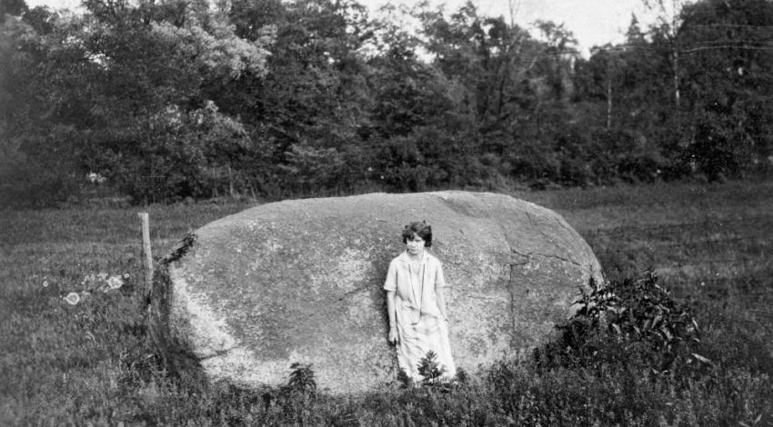 A black and white photo of a person standing in front of a large boulder