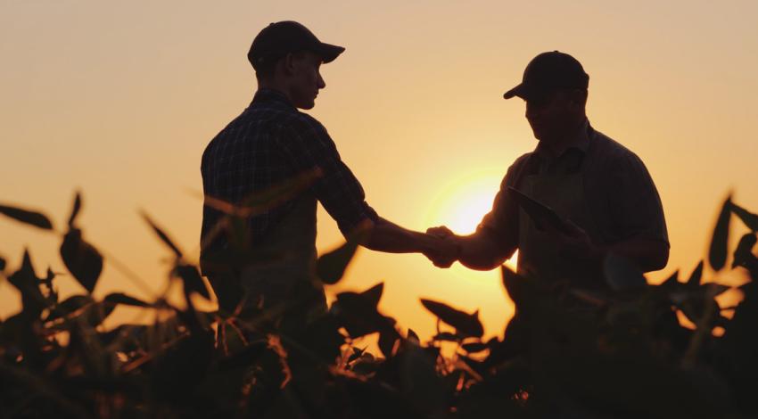 the silhouette of two people shaking hands in a farm field