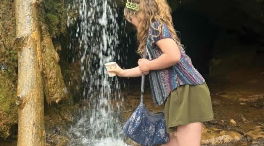 A girl holding a cup under a spring waterfall