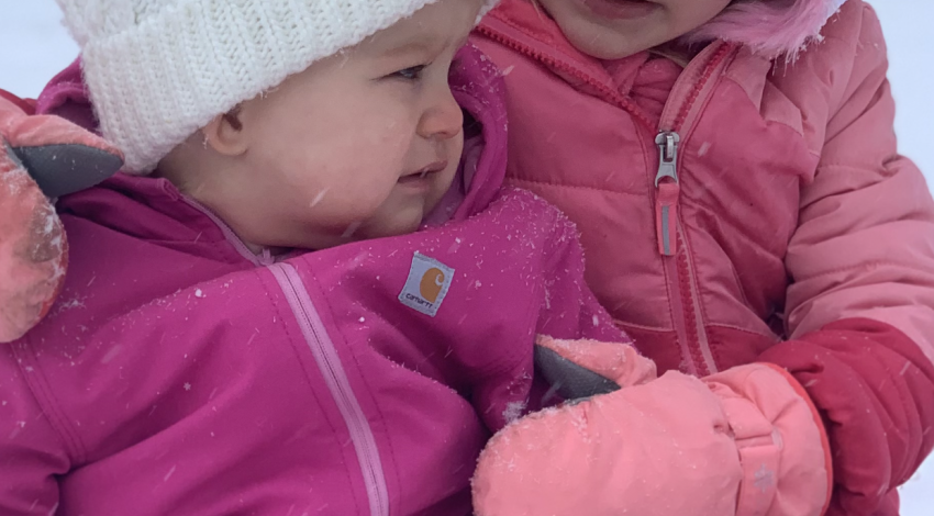 little girl and baby sitting in the snow