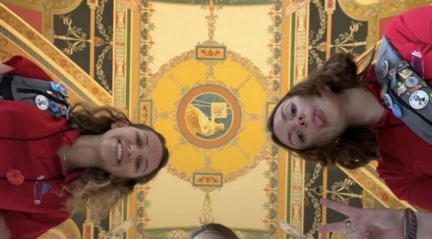 Photo of three teenage girls, shot from below, with ornate ceiling above