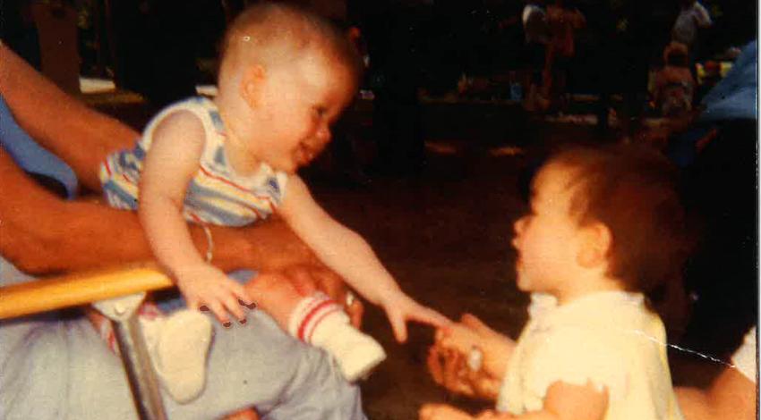 baby boy on lap reaches for little girl