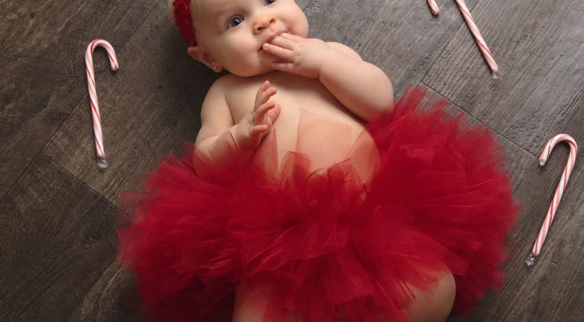 Baby girl in fluffy red tutu, ringed by candy canes and sucking on her fingers