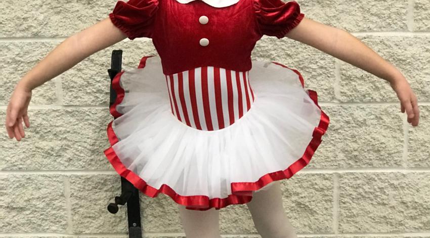 Young girl posing in dance costume with red-and-white striped body and red-trimmed white tutu