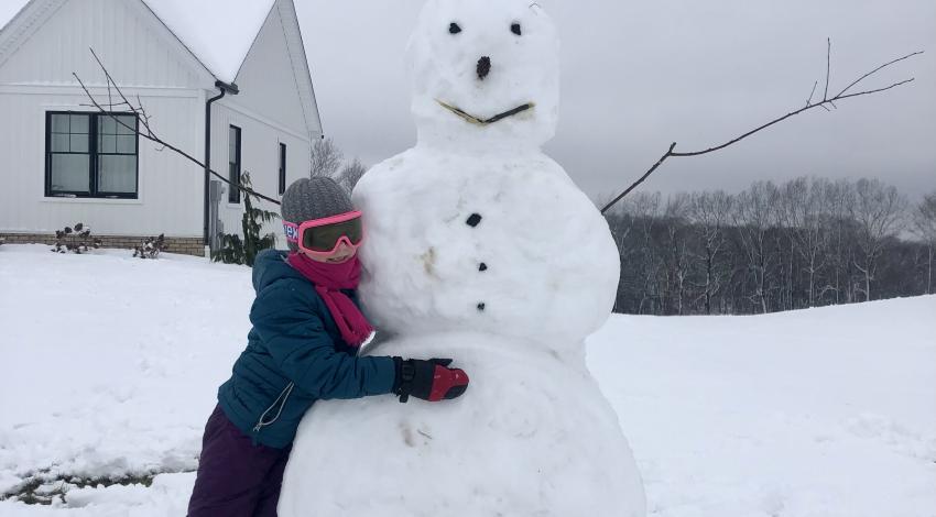 child hugs giant snowman