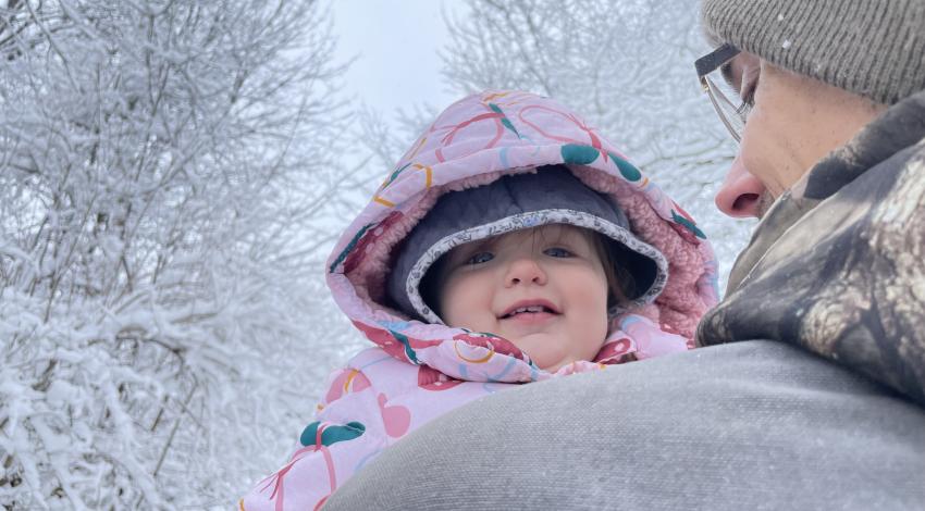 little girl looking over man's shoulder in front of snowy trees