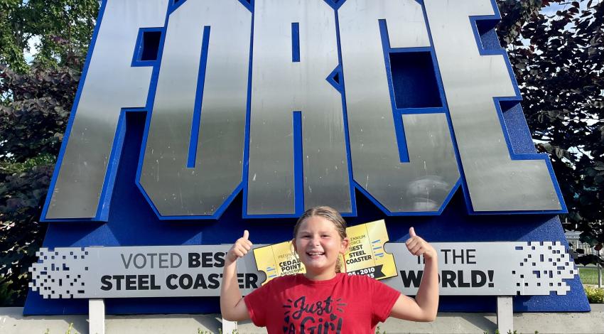 kid standing in front of roller coaster sign