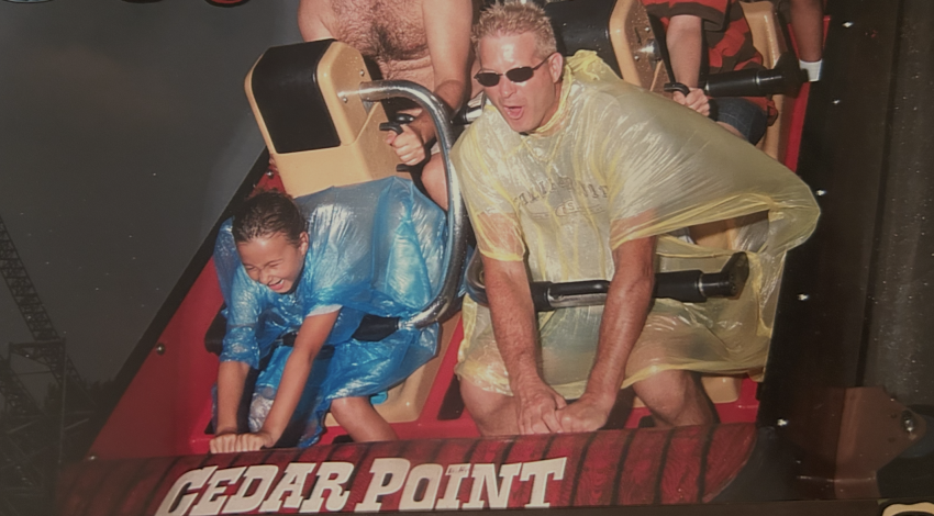 man and child in ponchos on roller coaster