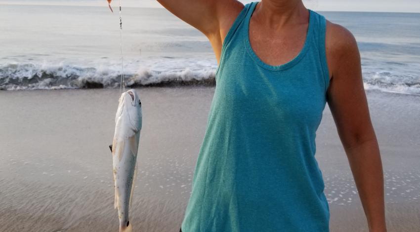 woman smiling while holding up a fish