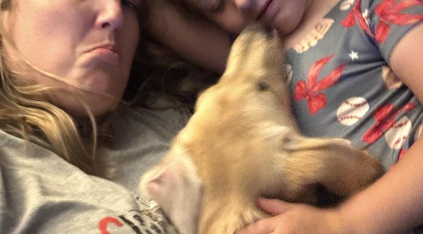 Woman, girl, and dog snuggled on couch