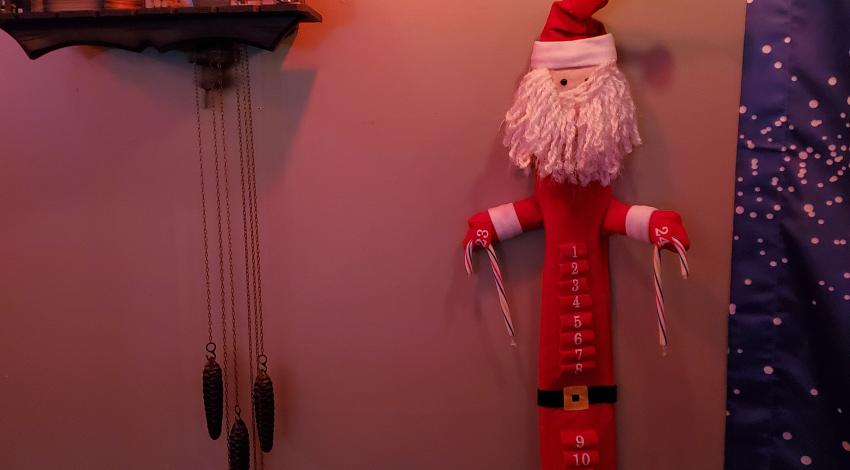 Long fabric Santa Advent Calendar, with two candy canes left at the bottom, hangs on the wall beside cuckoo clock.