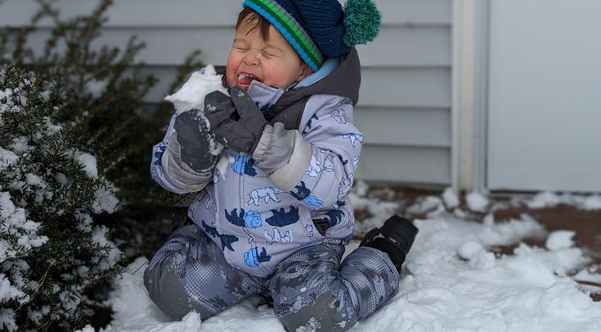 Toddler in snow suit, eating snow