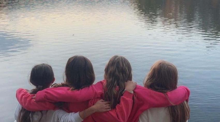 group of girls with arms around each other on edge of lake