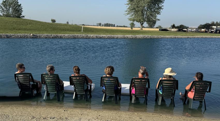 people sitting in chairs in shallow water along lake's edge