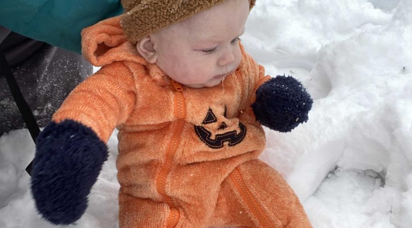 small baby in pumpkin outfit sitting in the snow