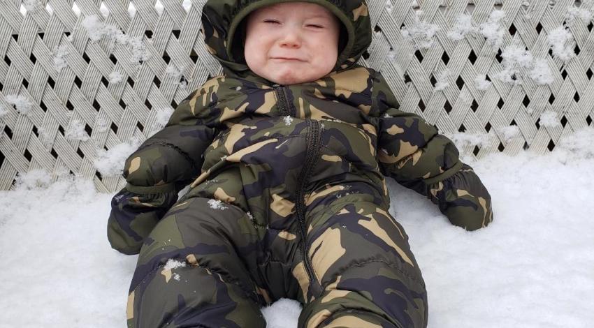 baby in snowsuit on snow-covered bench