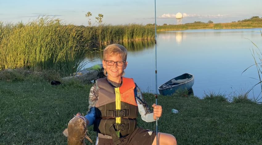 smiling boy kneels while holding fish and pole