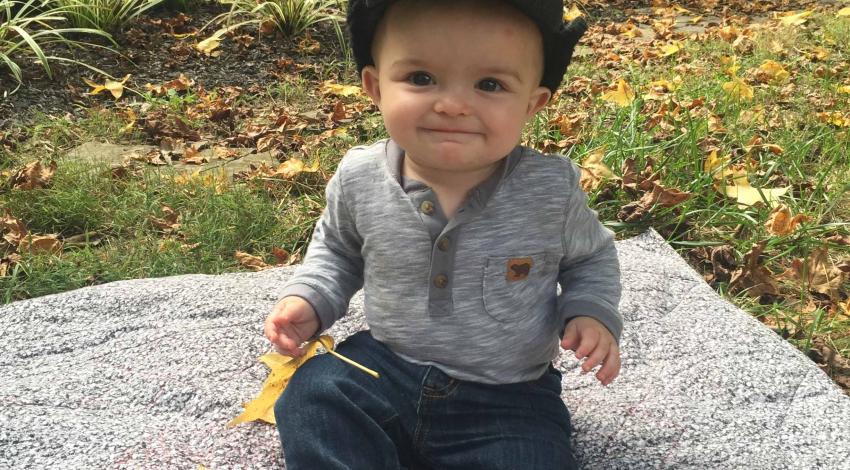 smiling baby sits near fallen leaves