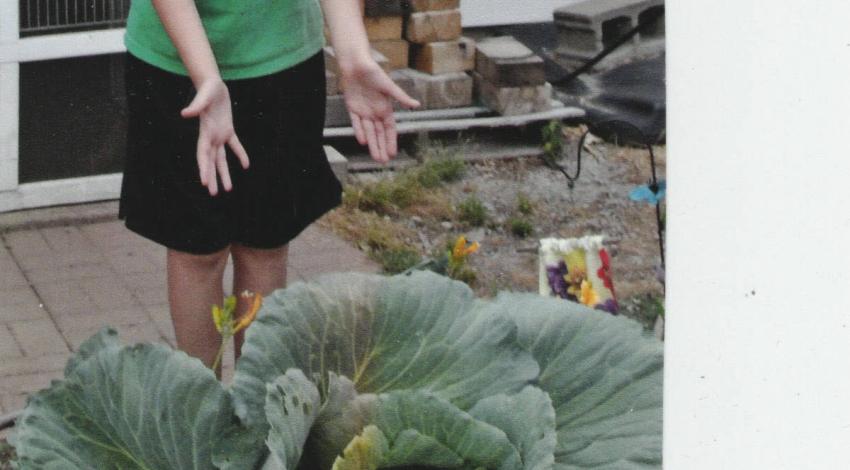 blond boy stands behind very large green plant
