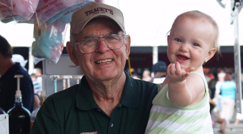 Older man in hat holds smiling baby in front of cotton candy