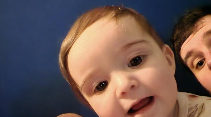 baby looking into camera, man in back