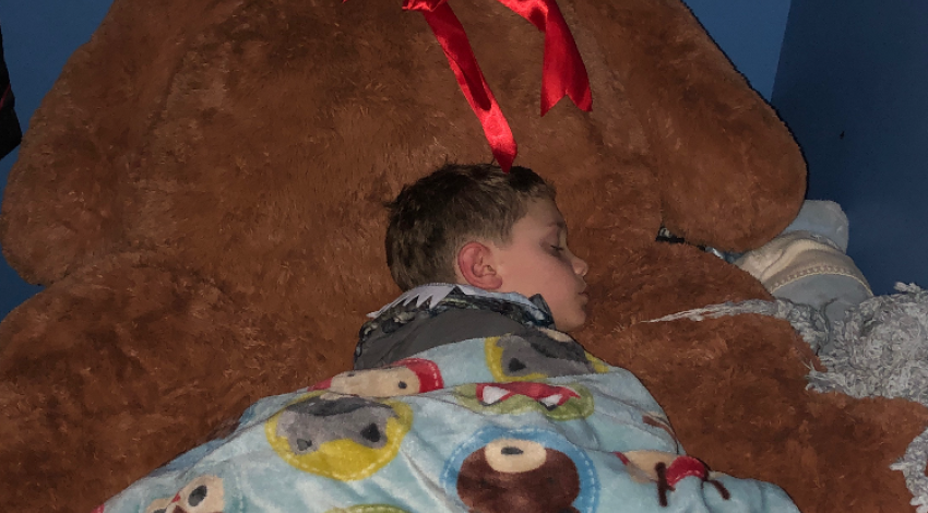 Small boy sleeping against giant teddy bear