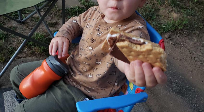 toddler boy on folding chair holds up s'more