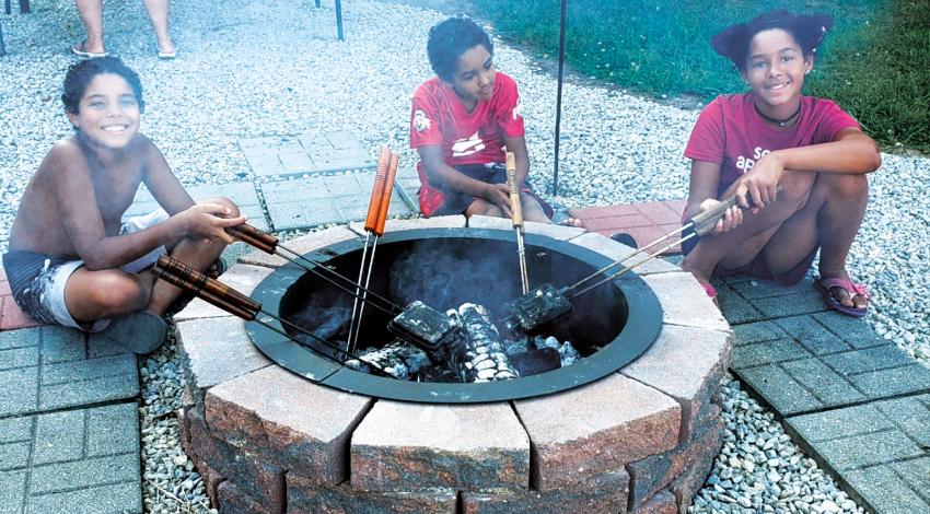 three smiling children roast marshmallows over a campfire