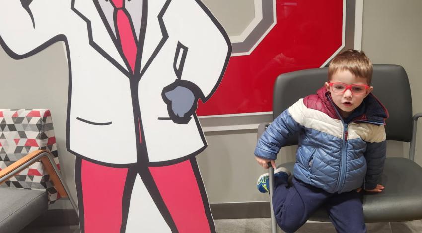 little boy next to buckeye mascot cutout - both wearing glasses