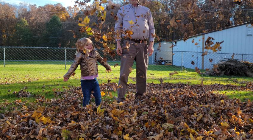 little girl tosses leaves in leaf pile while man watches